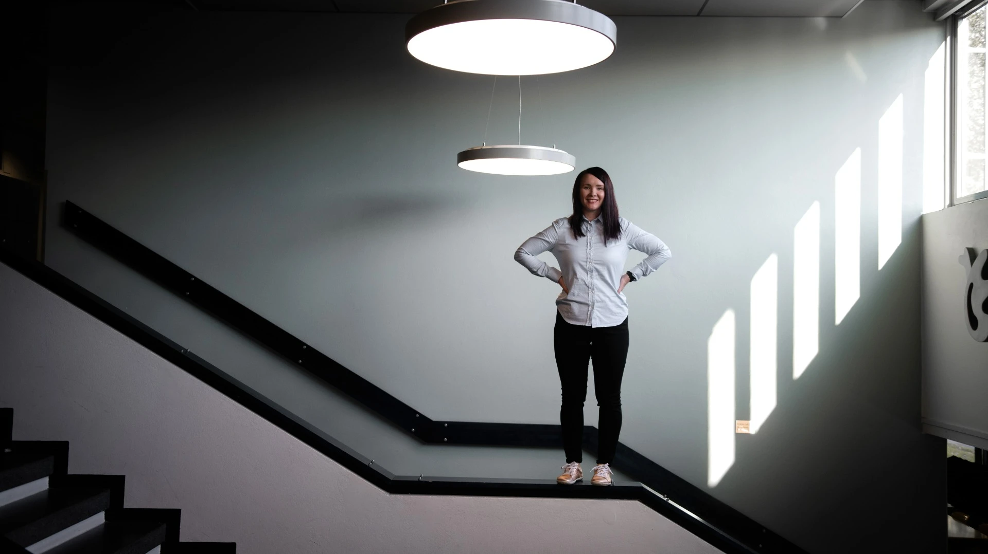 Riikka Koronsalmi seisomassa portaiden kaiteella hymyillen.